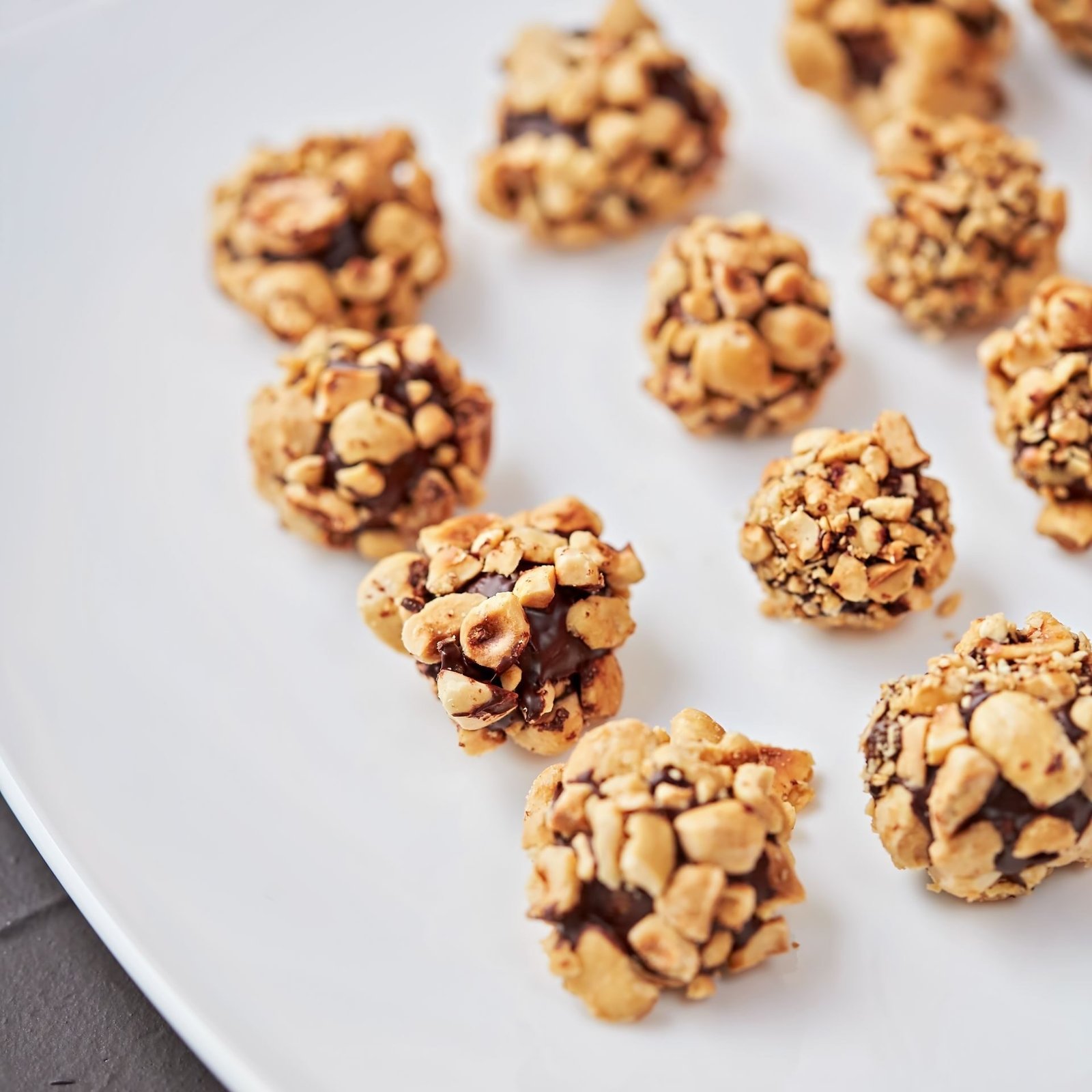 Close-up of hazelnut chocolate truffles coated in chopped nuts on a white plate.