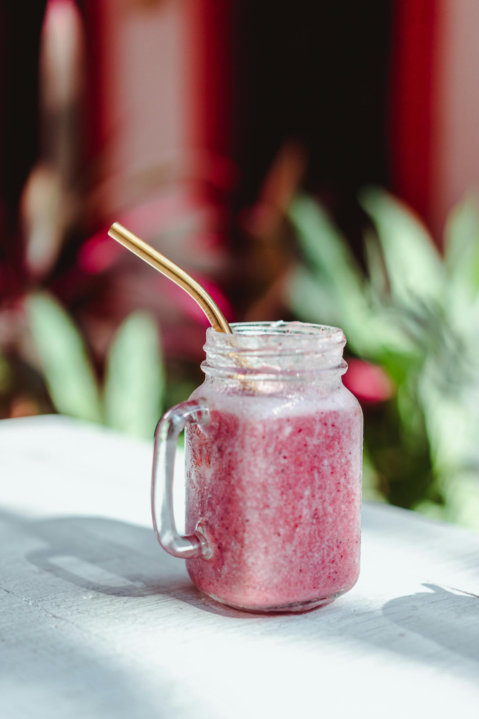 Delicious strawberry smoothie in a glass jar with a straw, perfect for a refreshing summer drink.