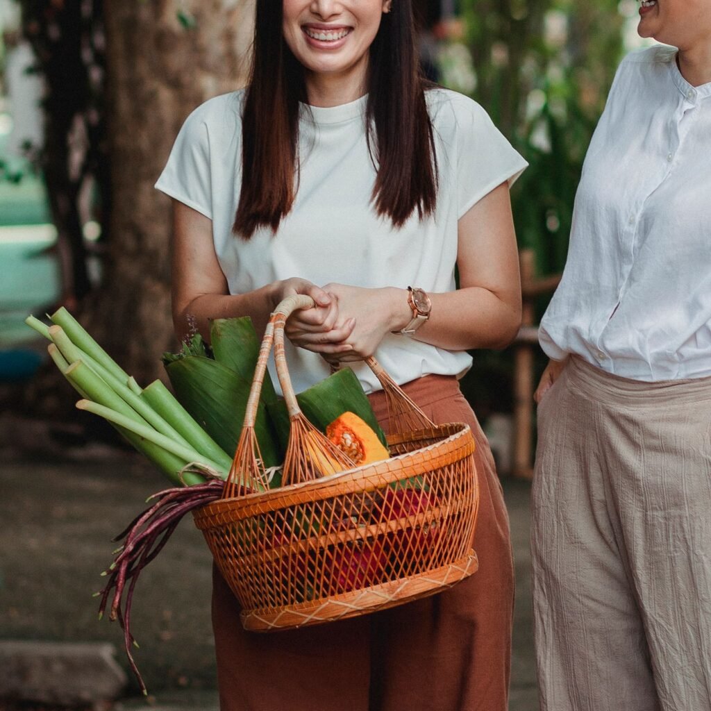 Crop unrecognizable glad woman with hand in pocket near partner with basket full of vegetables conversing in town