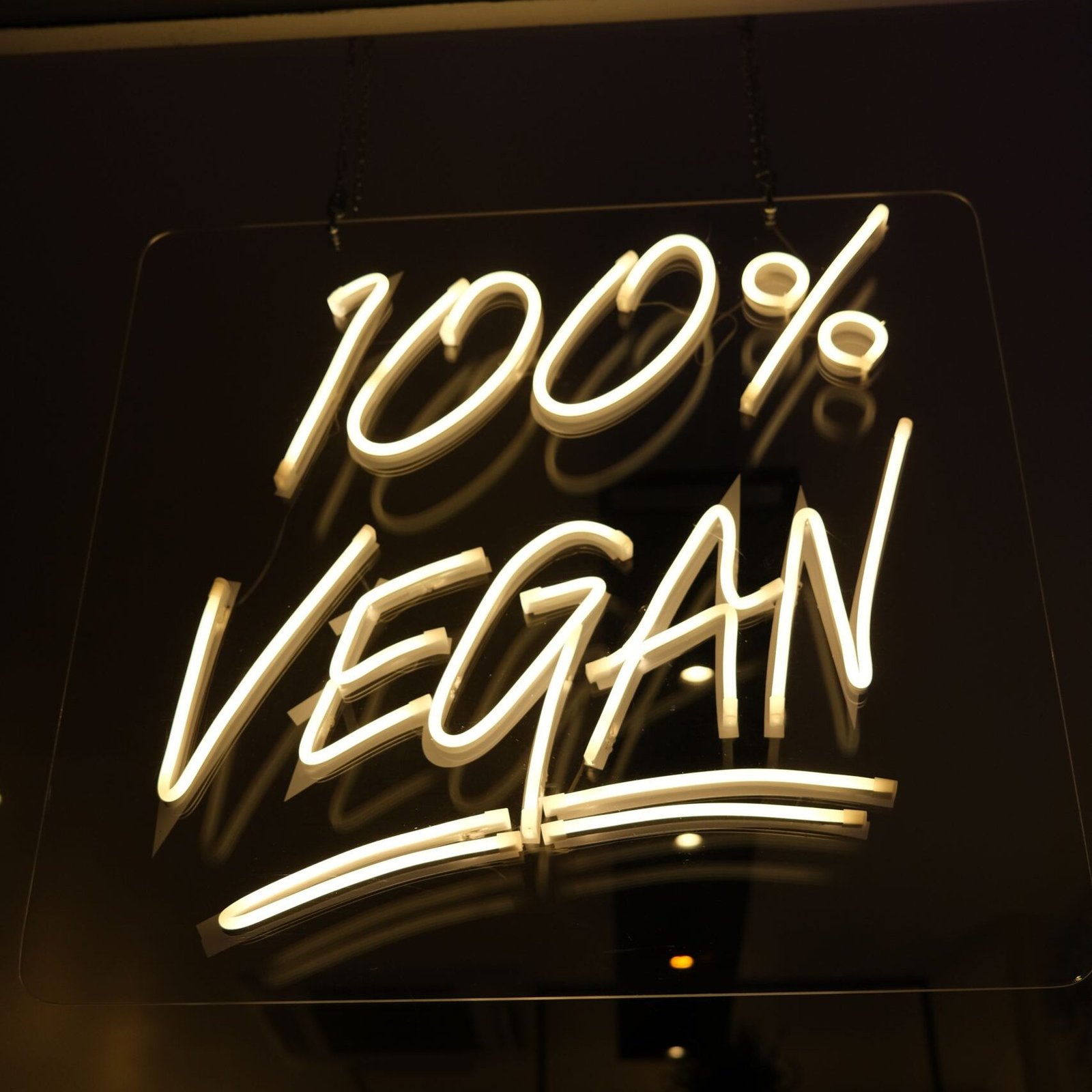 Glowing '100% Vegan' neon sign at a chic vegan restaurant, reflecting commitment to healthy eating.