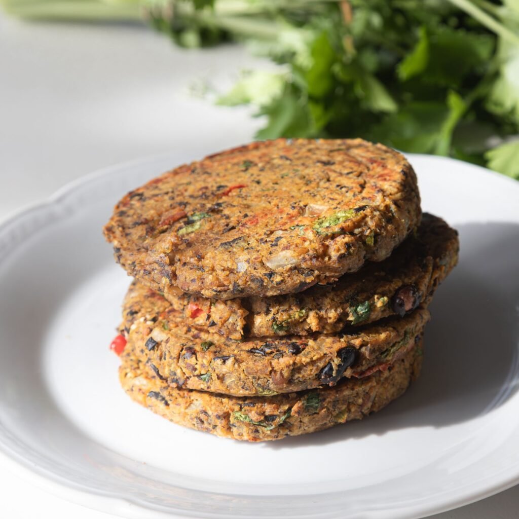 Stack of homemade vegetarian burger patties on a plate with fresh herbs in the background.