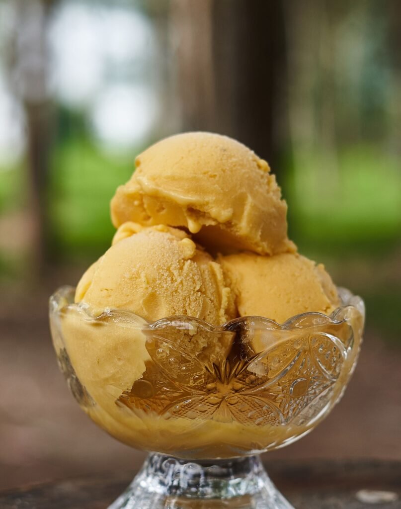 Creamy yellow ice cream scoops in elegant glass bowl, perfect sweet treat.