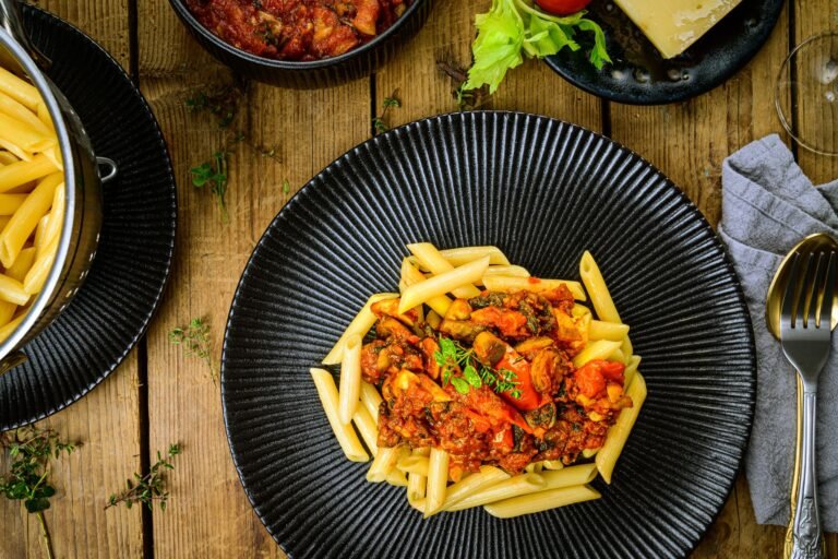 A delectable plate of penne pasta topped with rich tomato sauce, served on a rustic wooden table.
