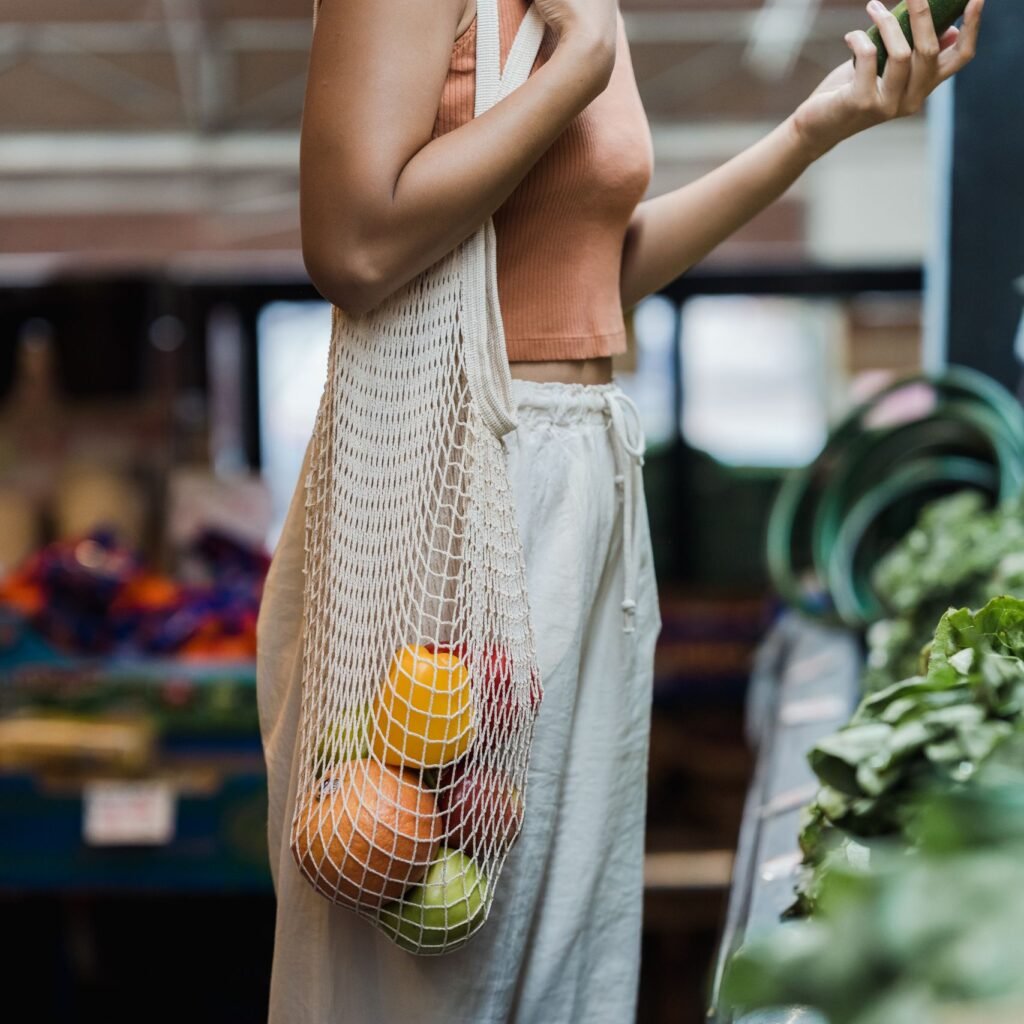 A woman shopping at a market with a mesh tote bag filled with fruits. Eco-friendly lifestyle.