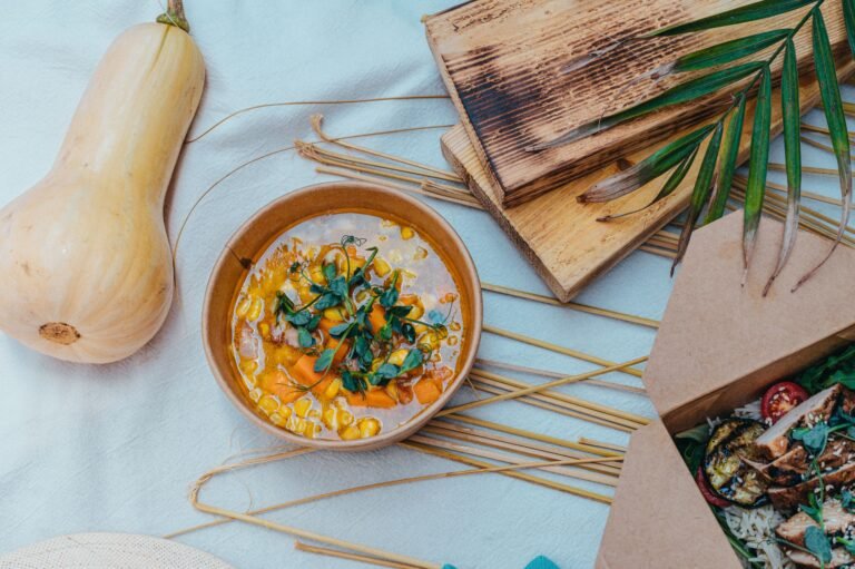 A cozy flat lay of a rustic table setting featuring a bowl of pumpkin soup and grilled food.